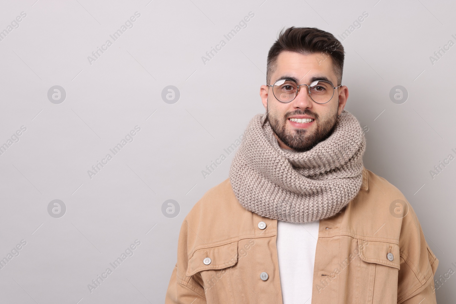 Photo of Smiling man in warm scarf on light grey background. Space for text