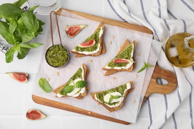 Photo of Tasty bruschettas with cream cheese, pesto sauce, figs and fresh basil on white table, flat lay