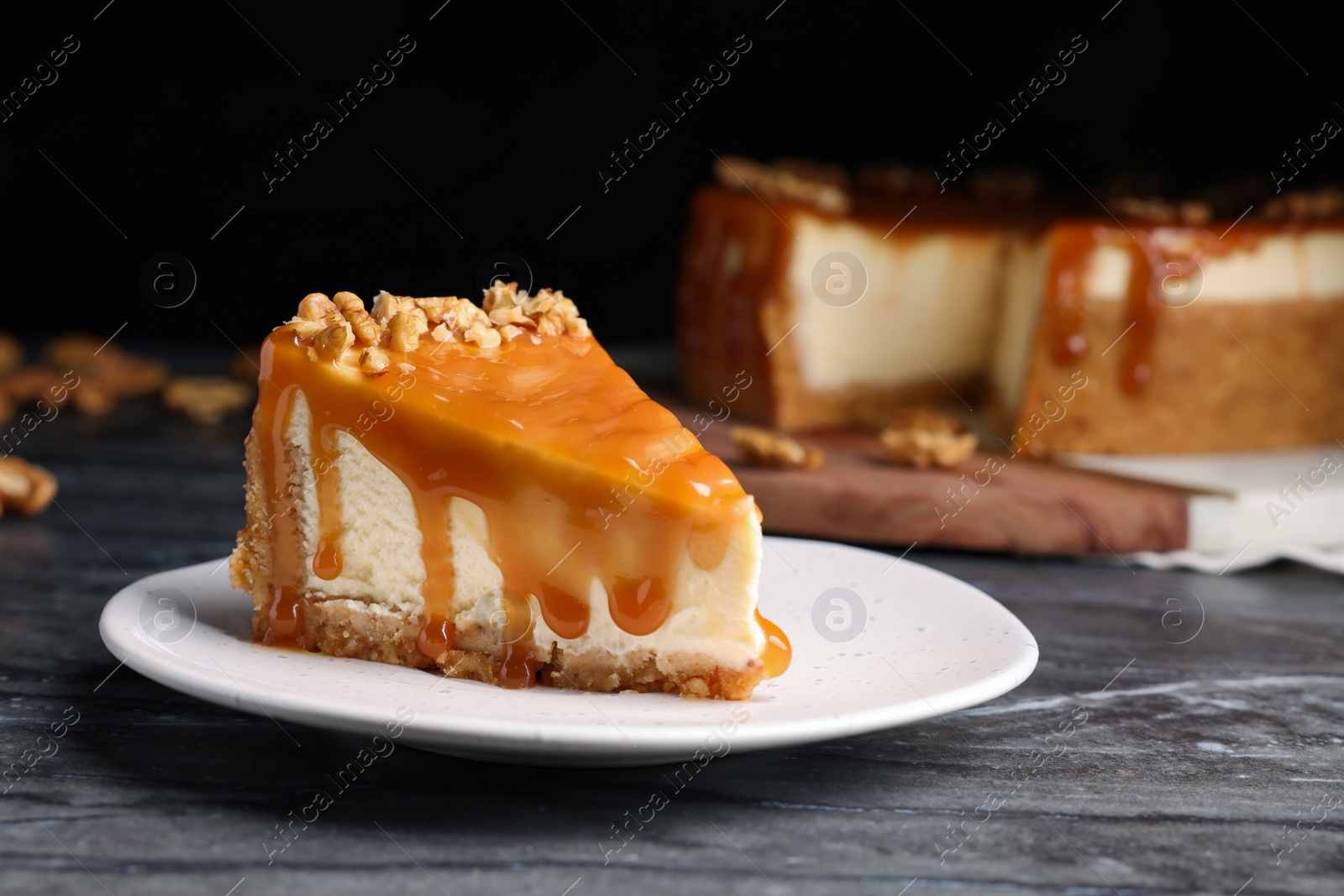 Photo of Piece of delicious cake with caramel and walnuts on black marble table, space for text