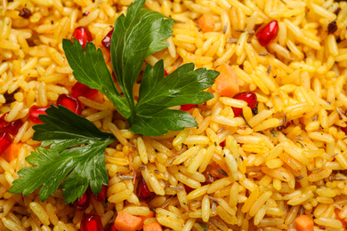 Photo of Tasty rice pilaf with pomegranate grains and parsley as background, closeup