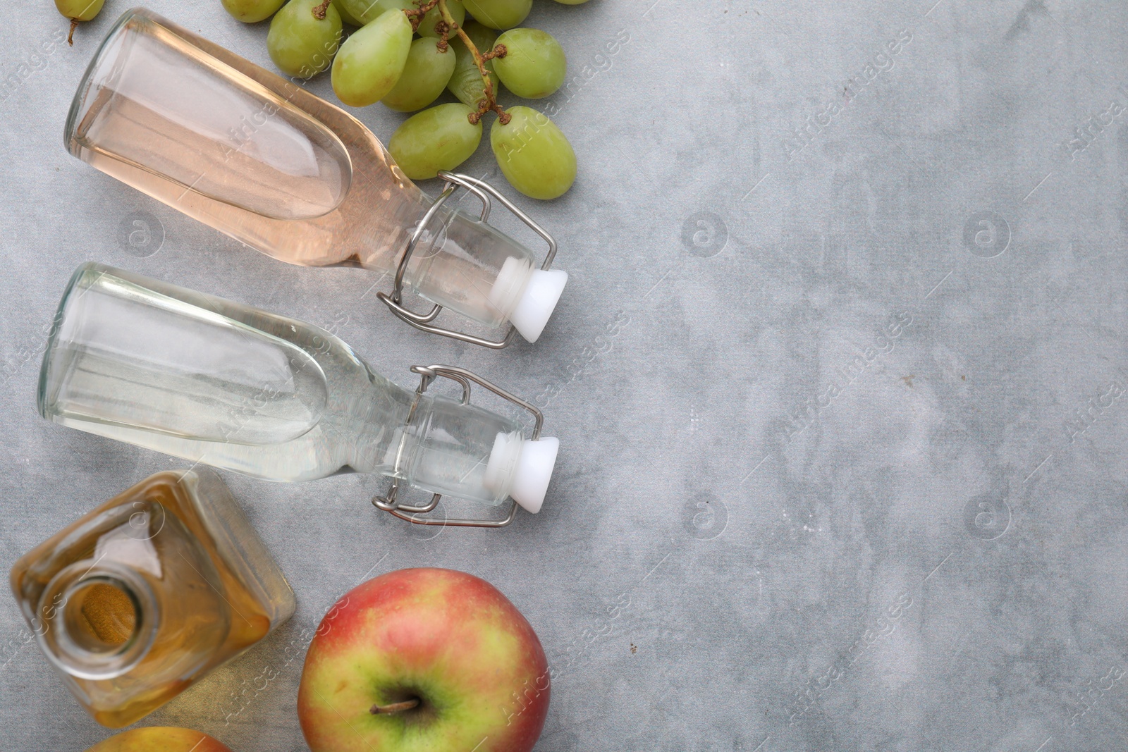 Photo of Different types of vinegar and fresh fruits on grey table, flat lay. Space for text