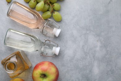 Different types of vinegar and fresh fruits on grey table, flat lay. Space for text