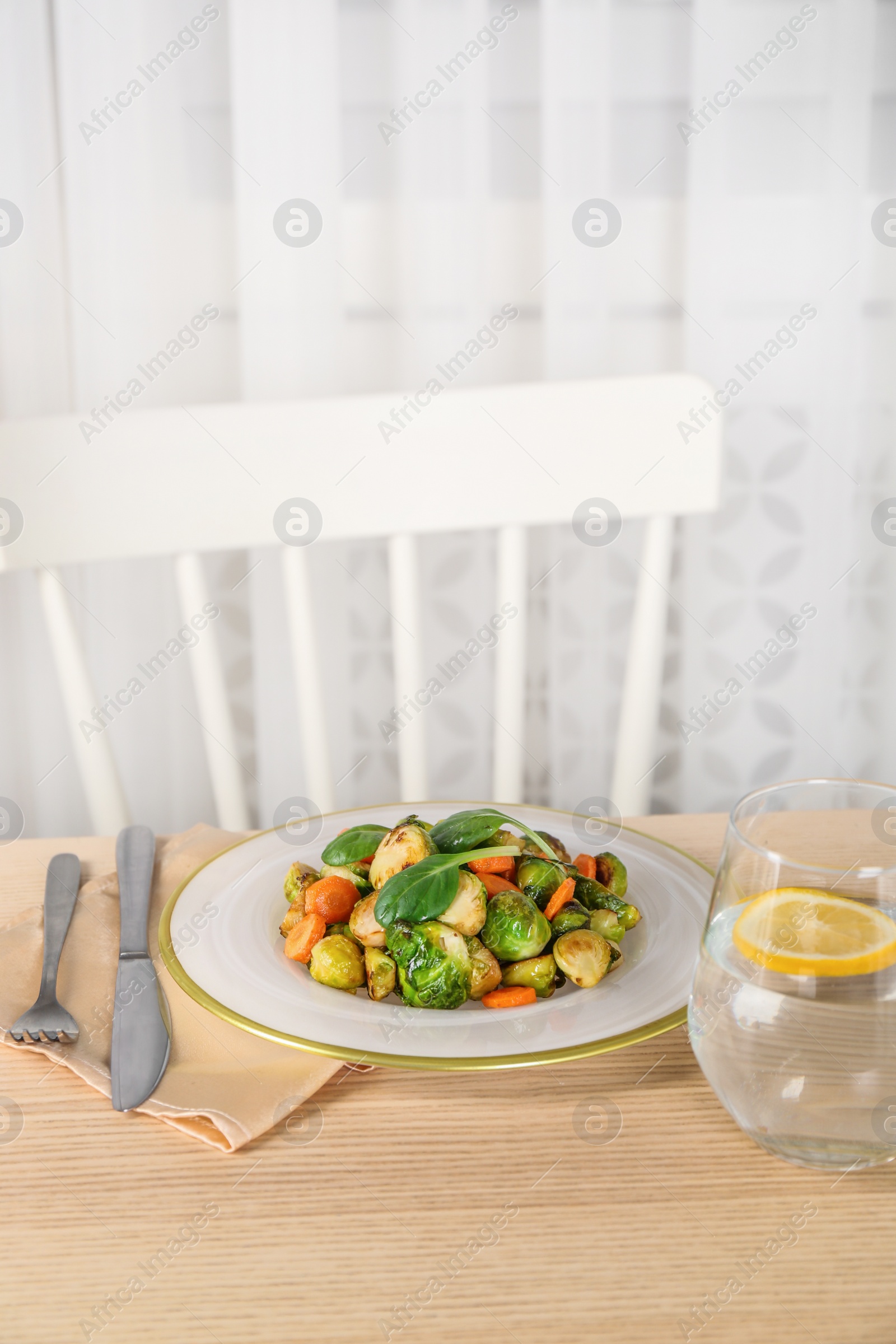 Photo of Delicious roasted Brussels sprouts and water with lemon served on wooden table indoors