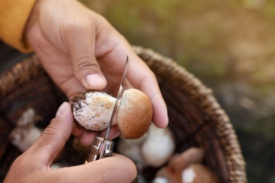 Photo of Man peeling mushroom with knife over basket outdoors, closeup