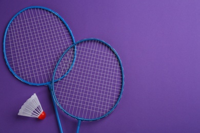Photo of Badminton rackets and shuttlecock on purple background, flat lay. Space for text
