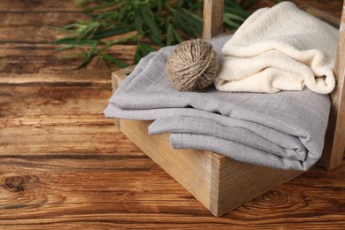 Photo of Hemp cloths and woolen yarn in crate on wooden table, space for text