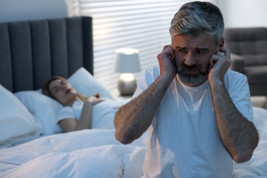 Photo of Irritated man covering his ears in bed at home, space for text. Problem with snoring wife