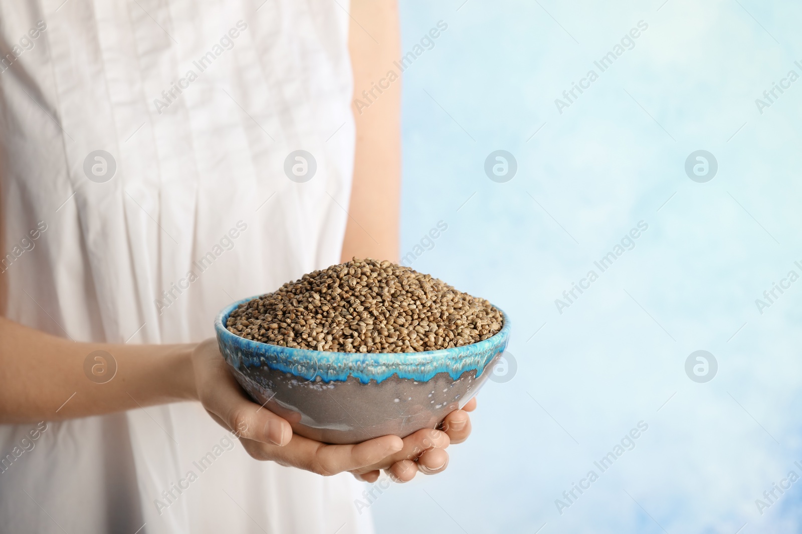 Photo of Woman holding bowl with hemp seeds on color background, closeup