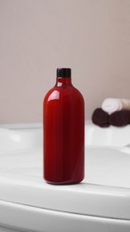 Photo of Red bottle of bubble bath and towels on tub indoors