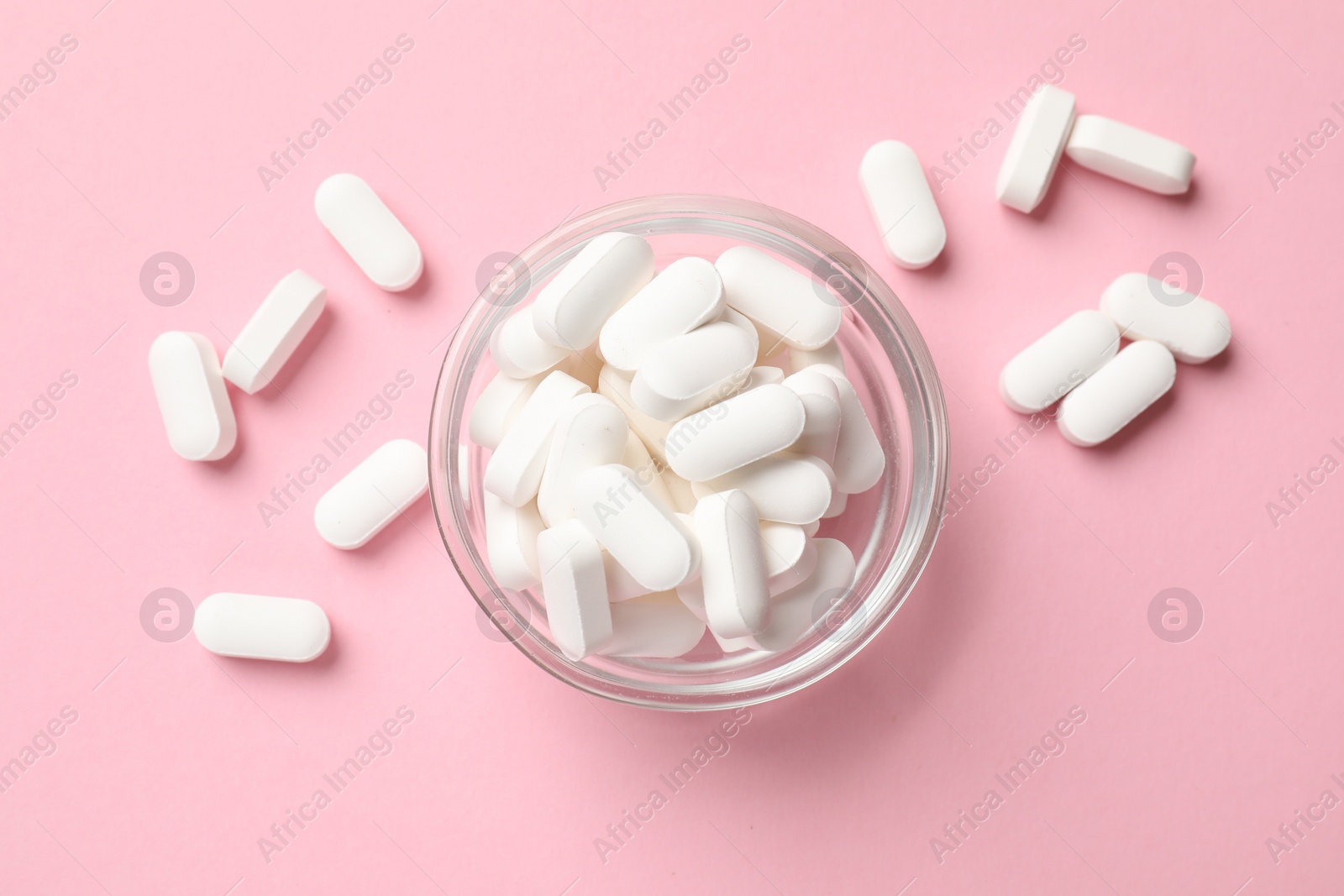 Photo of Vitamin capsules in bowl on pink background, top view