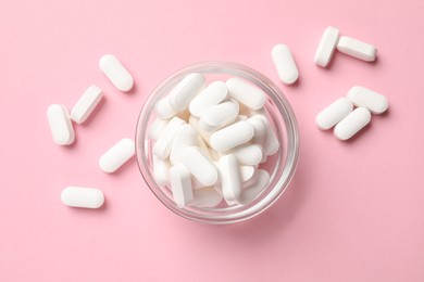 Photo of Vitamin capsules in bowl on pink background, top view