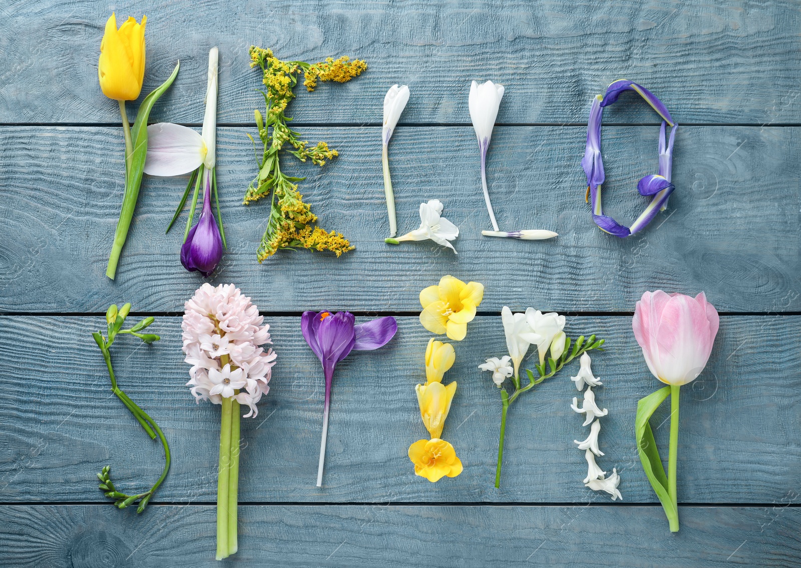 Photo of Words HELLO SPRING made of fresh flowers on light blue wooden table, flat lay