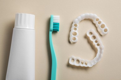Photo of Toothpaste, brush and dental mouth guards on beige background, flat lay. Bite correction
