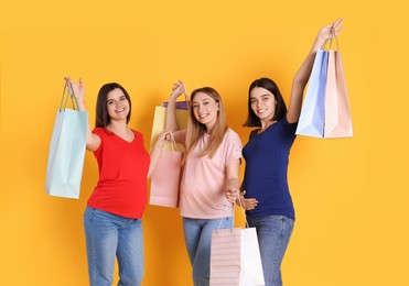 Happy pregnant women with shopping bags on orange background