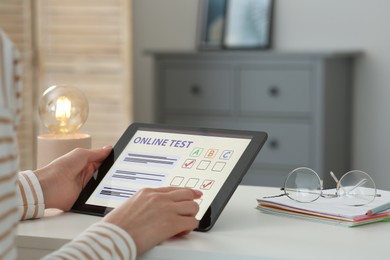 Woman taking online test on tablet at desk indoors, closeup