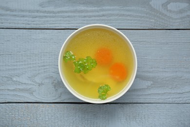 Photo of Delicious chicken bouillon with carrot and parsley on grey wooden table, top view