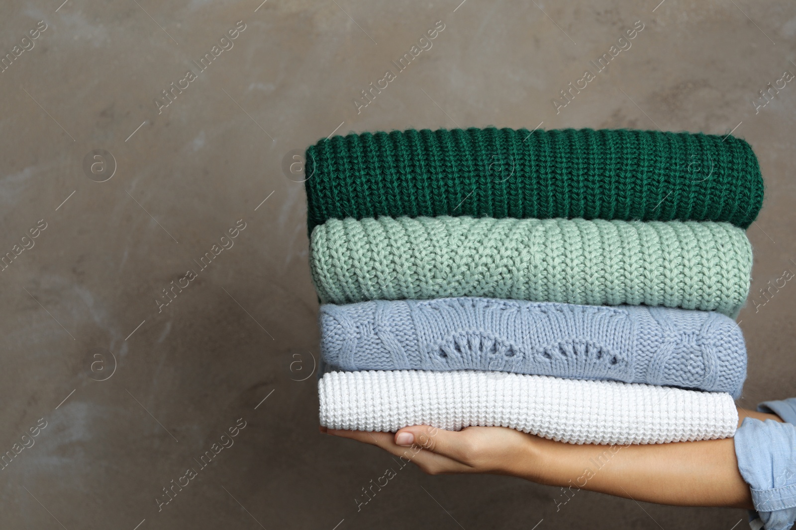 Photo of Woman holding stack of warm clothes on grey background, closeup. Autumn season