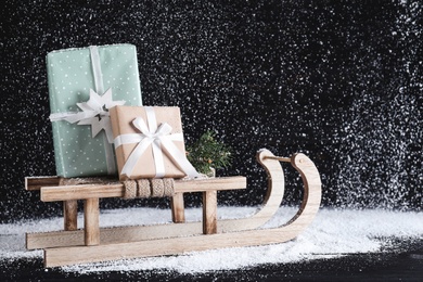 Photo of Sleigh with gift boxes on black wooden table during snowfall