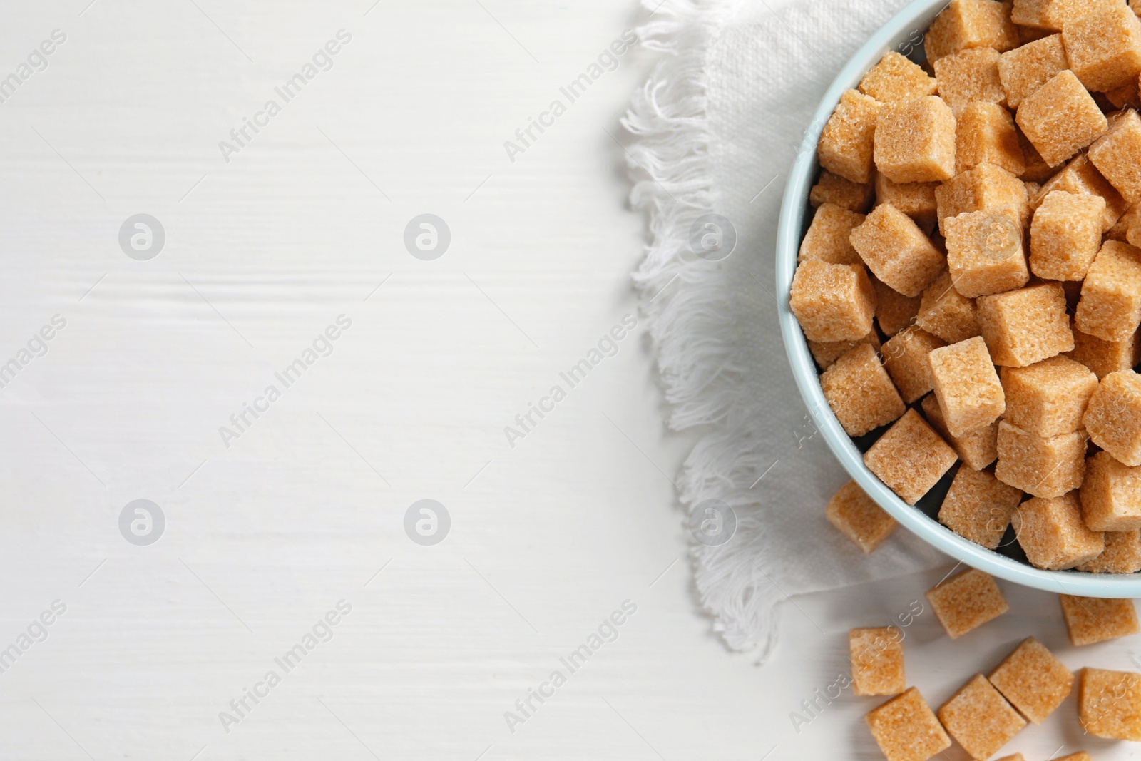 Photo of Bowl of brown sugar cubes on white wooden table, flat lay. Space for text