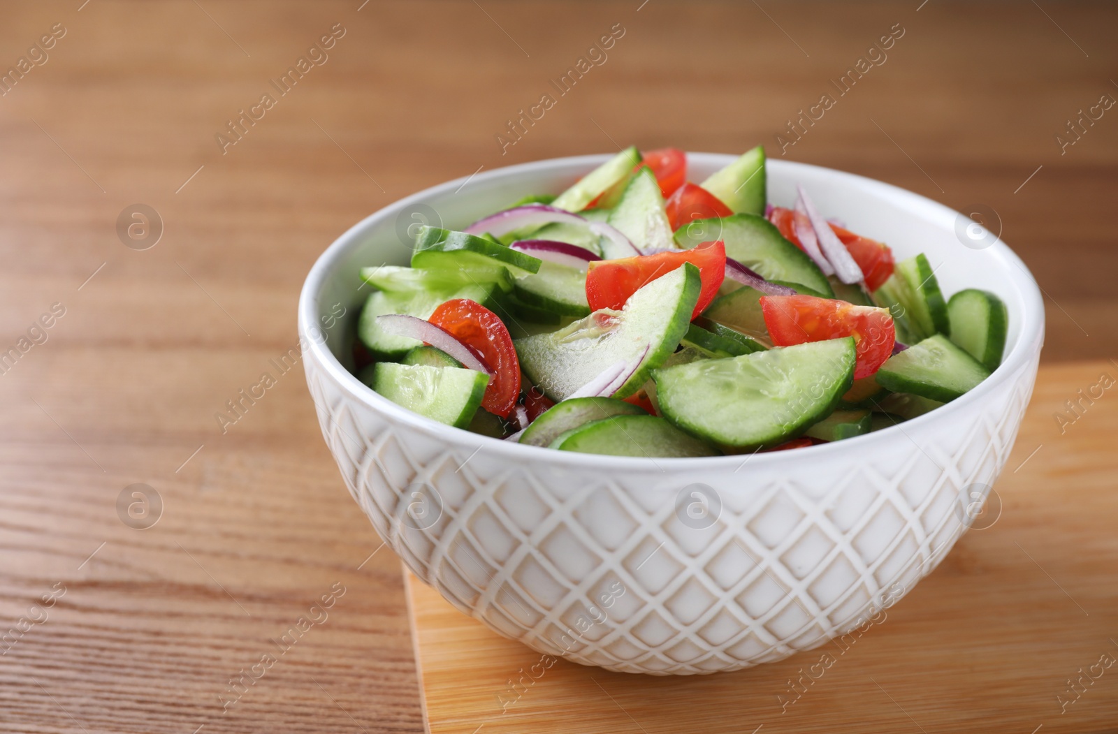 Photo of Bowl of tasty cucumber tomato salad on wooden table