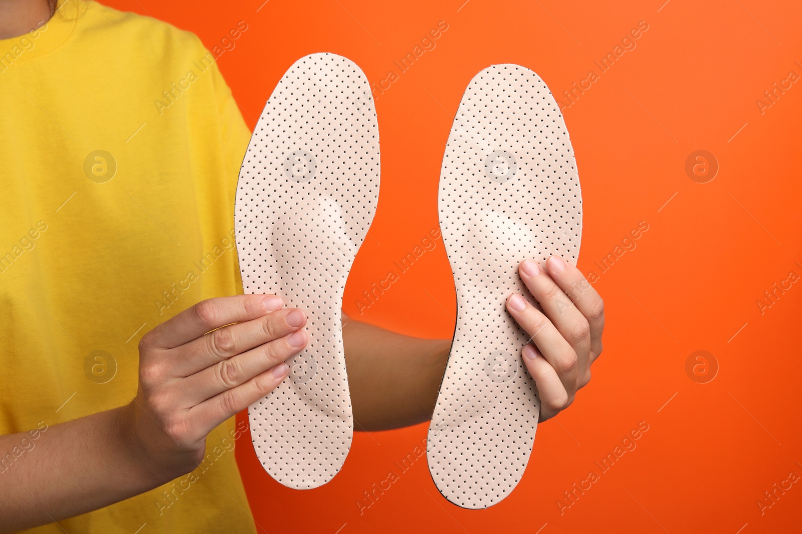 Photo of Woman holding beige orthopedic insoles on orange background, closeup