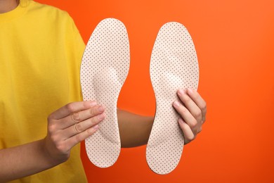 Photo of Woman holding beige orthopedic insoles on orange background, closeup