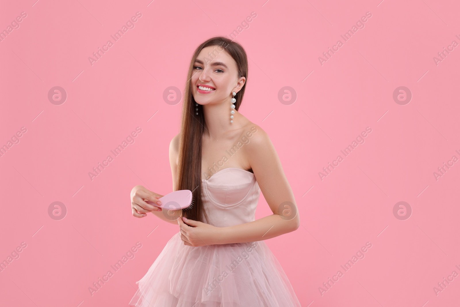 Photo of Beautiful woman in pale pink clothes brushing her hair on color background