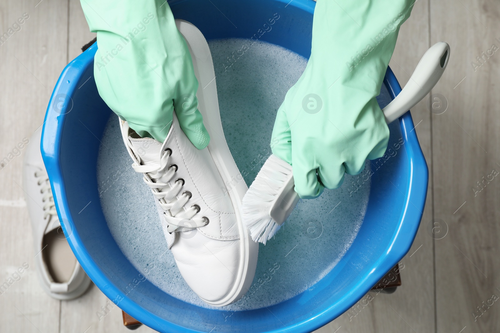 Photo of Woman with gloves and brush cleaning stylish sneakers in wash basin, top view