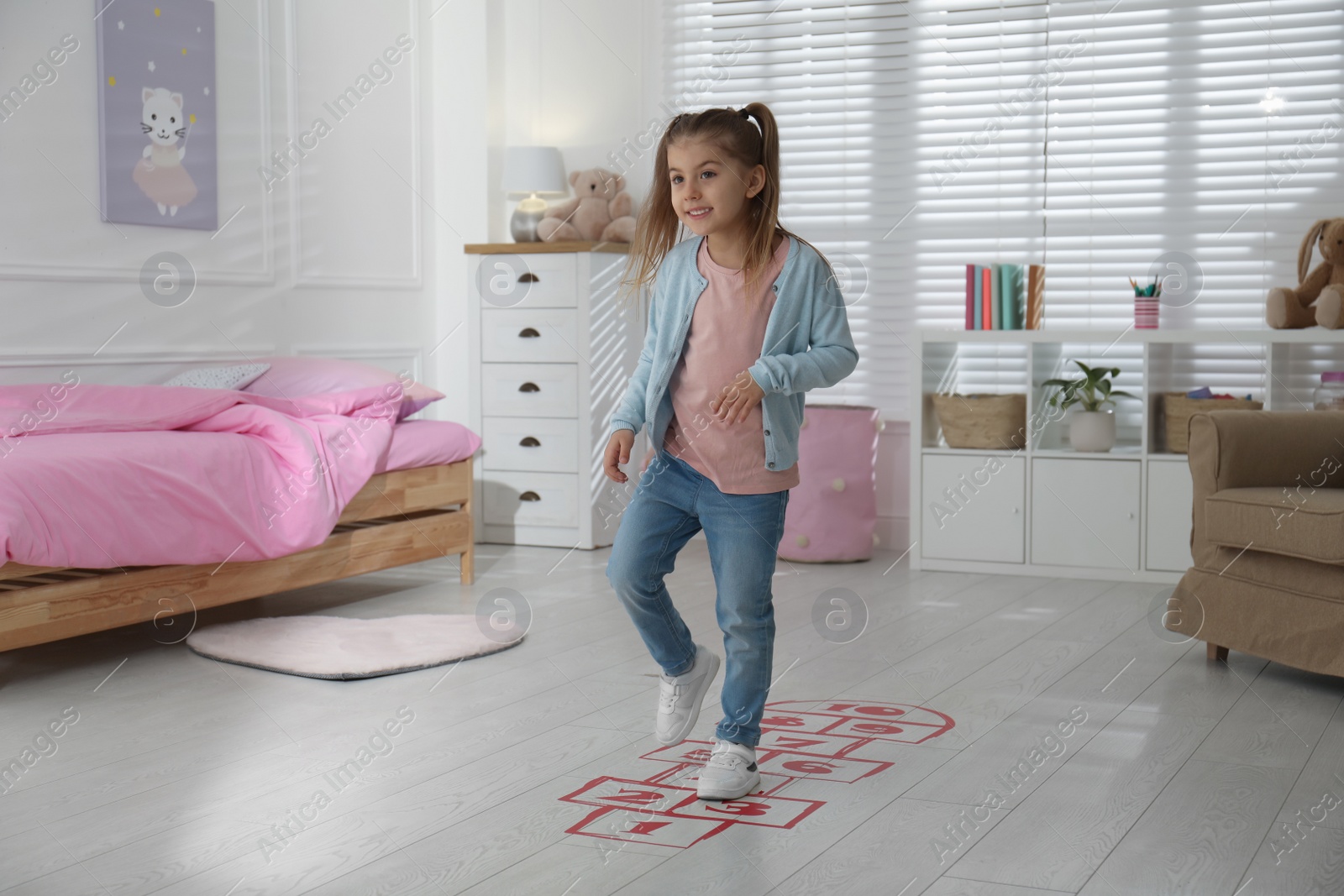 Photo of Cute little girl playing hopscotch at home