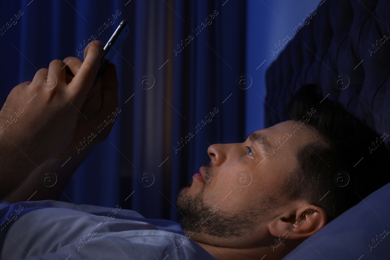 Photo of Handsome man using smartphone in dark room at night. Bedtime