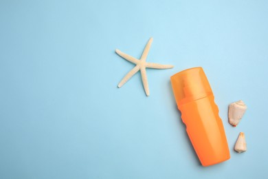 Bottle of sunscreen, starfish and seashells on light blue background, flat lay. Space for text