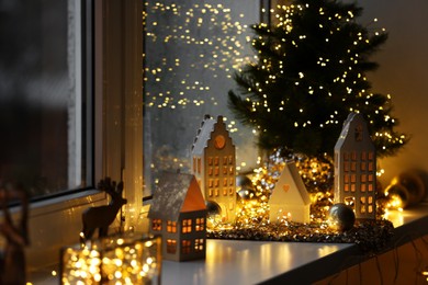 Photo of Beautiful decorative houses, baubles and small Christmas tree on window sill indoors