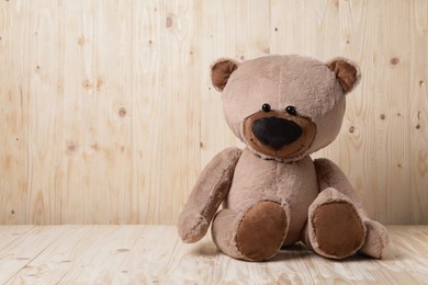 Photo of Cute teddy bear on table near wooden wall, space for text