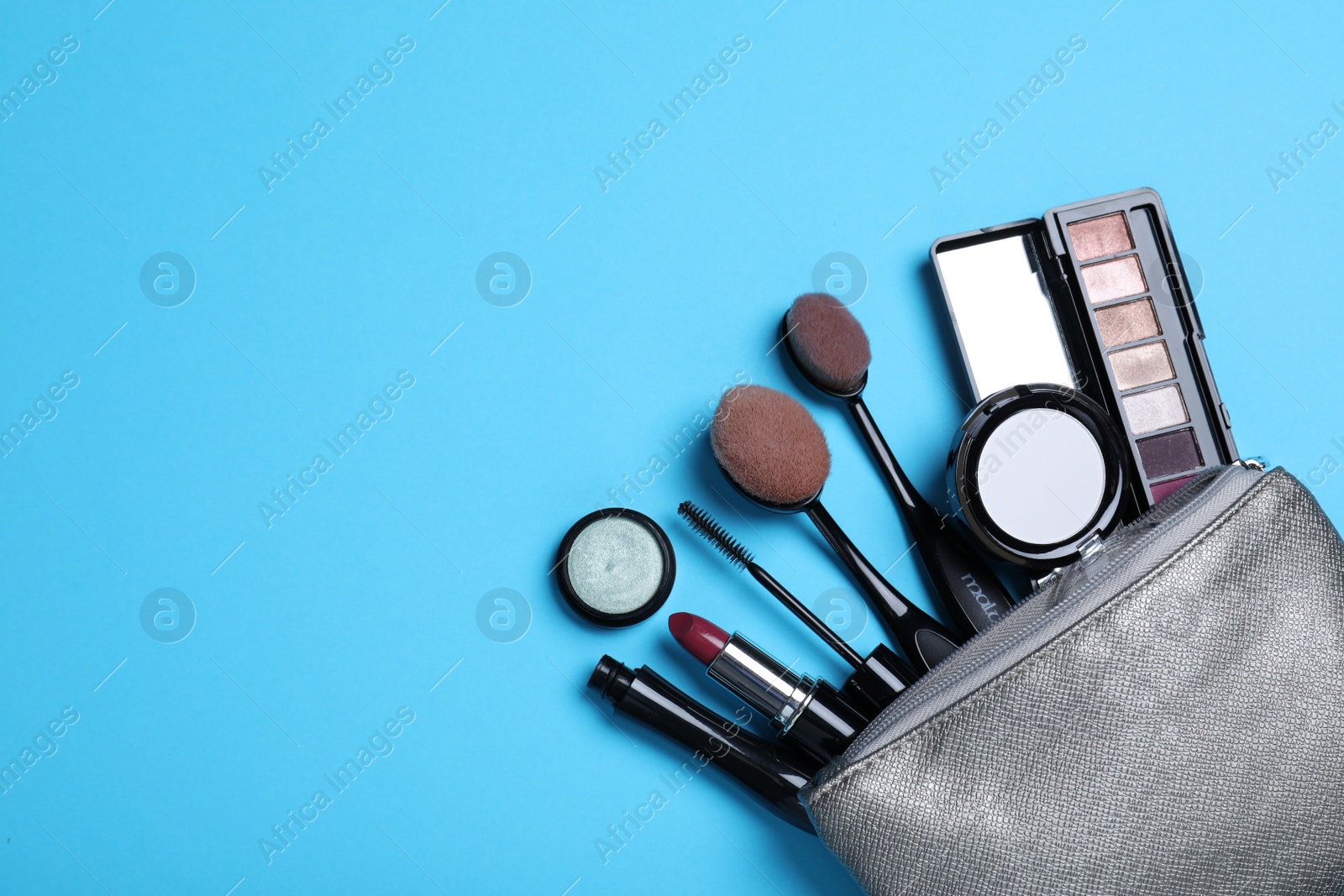 Photo of Cosmetic bag with makeup products and accessories on light blue background, flat lay. Space for text