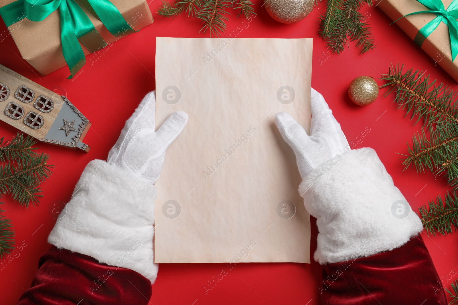 Photo of Santa Claus with blank paper and Christmas decor on red background, top view. Space for text