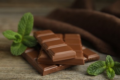 Tasty milk chocolate pieces with mint on wooden table, closeup