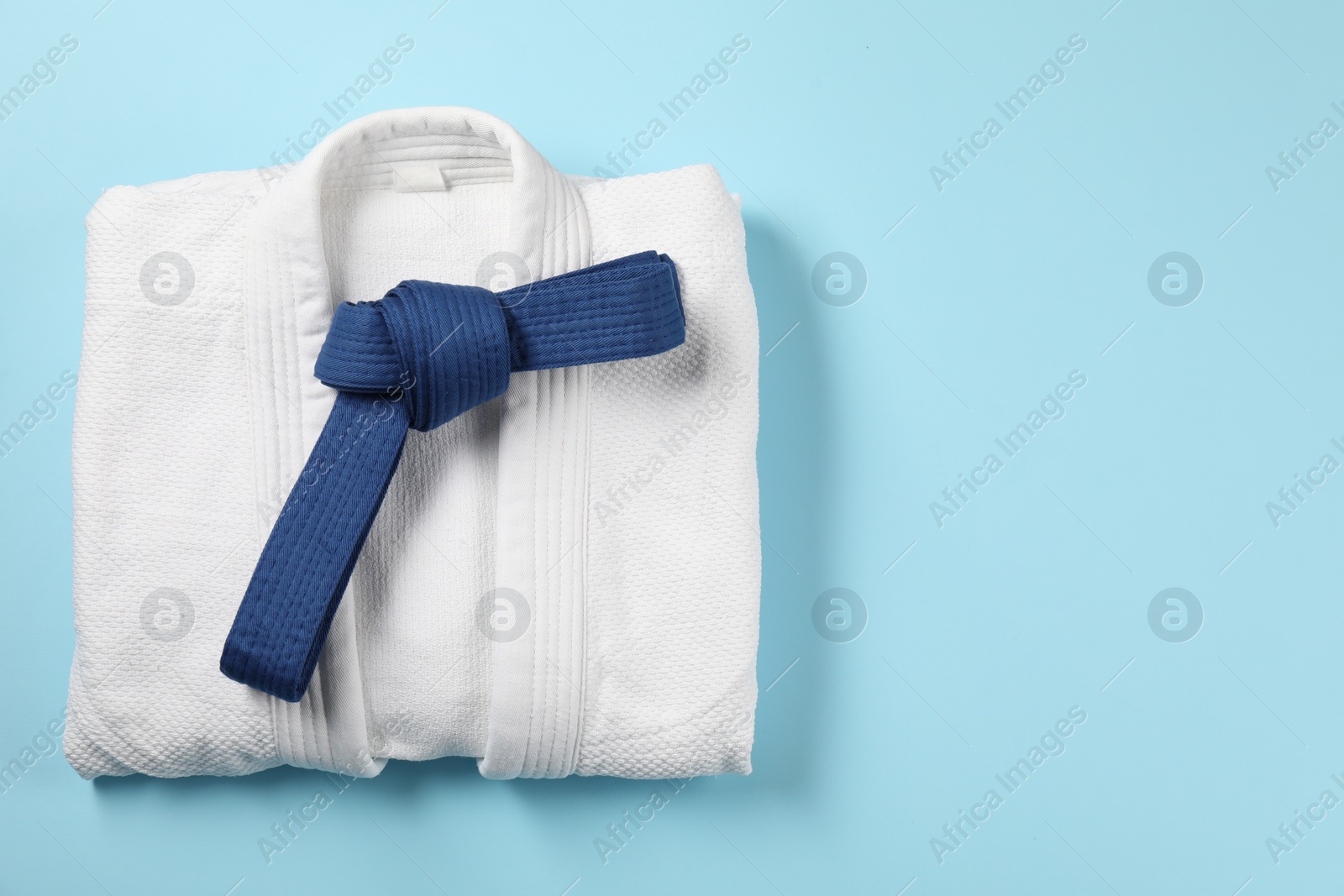 Photo of Karate belt and white kimono on light blue background, top view. Space for text