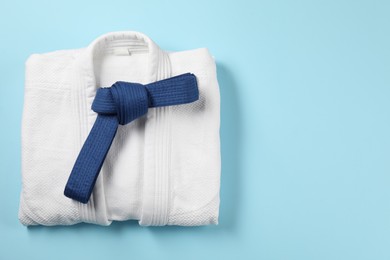 Karate belt and white kimono on light blue background, top view. Space for text