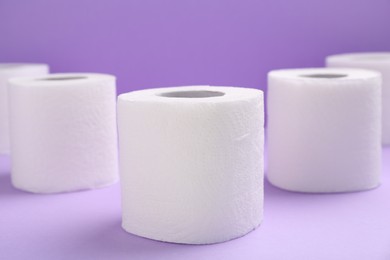 Photo of Soft toilet paper rolls on violet background, closeup