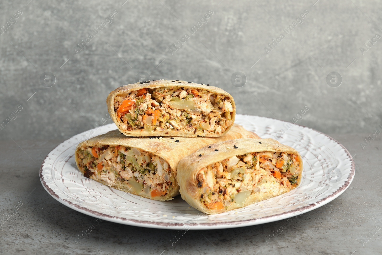 Photo of Pieces of delicious strudel with chicken and vegetables on light grey textured table, closeup