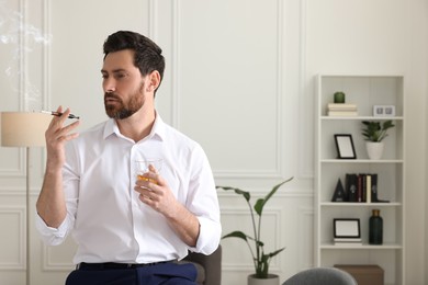 Photo of Man using cigarette holder for smoking and holding glass of whiskey in office