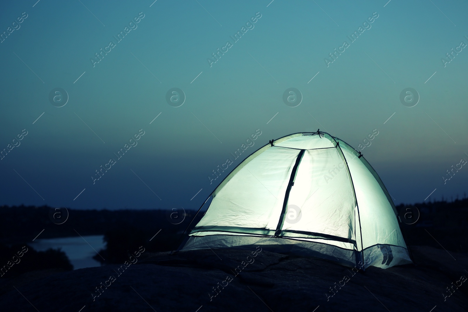 Photo of Small camping tent glowing in twilight outdoors. Space for text