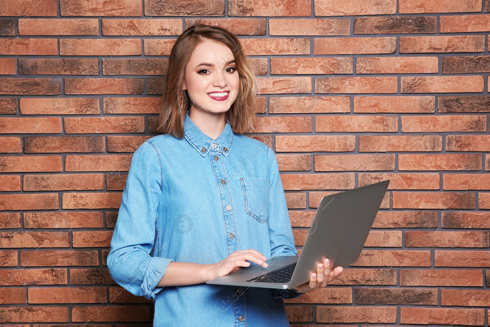 Photo of Beautiful young woman using laptop on brick wall background
