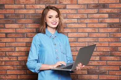 Photo of Beautiful young woman using laptop on brick wall background