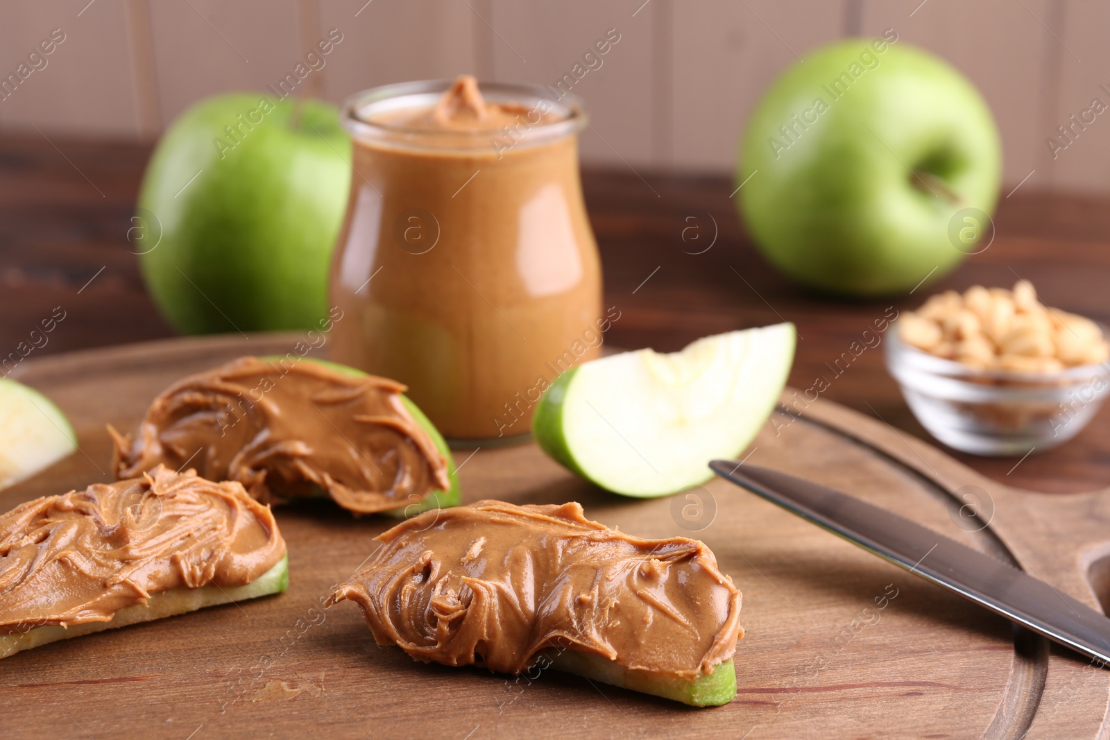 Photo of Slices of fresh green apple with peanut butter on wooden board, closeup