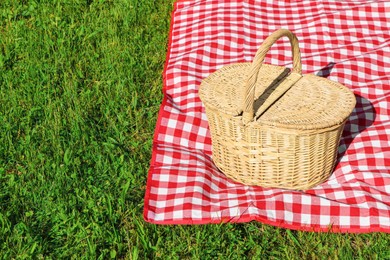 Photo of Picnic basket with checkered tablecloth on green grass outdoors, space for text