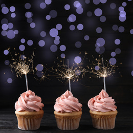 Birthday cupcakes with sparklers on wooden table against dark background