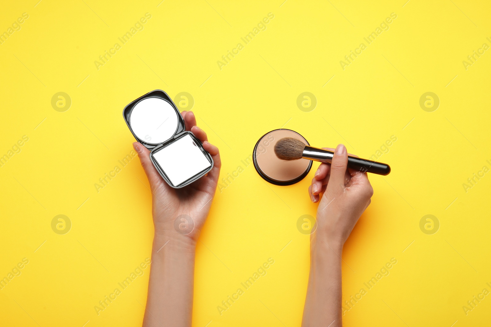 Photo of Woman holding pocket mirror and brush on yellow background, top view