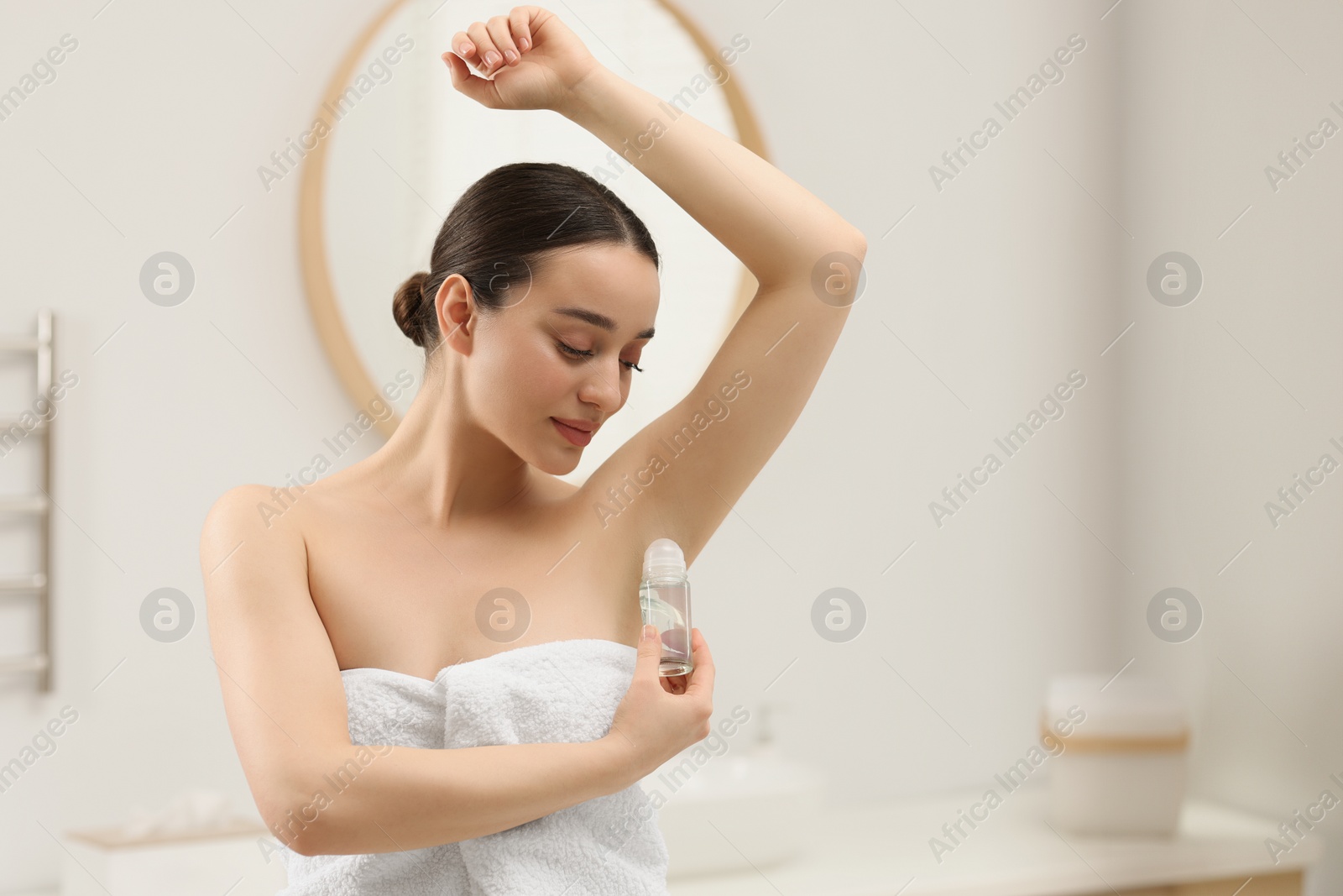 Photo of Beautiful young woman applying deodorant in bathroom