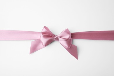 Pink satin ribbon with bow on white background, top view